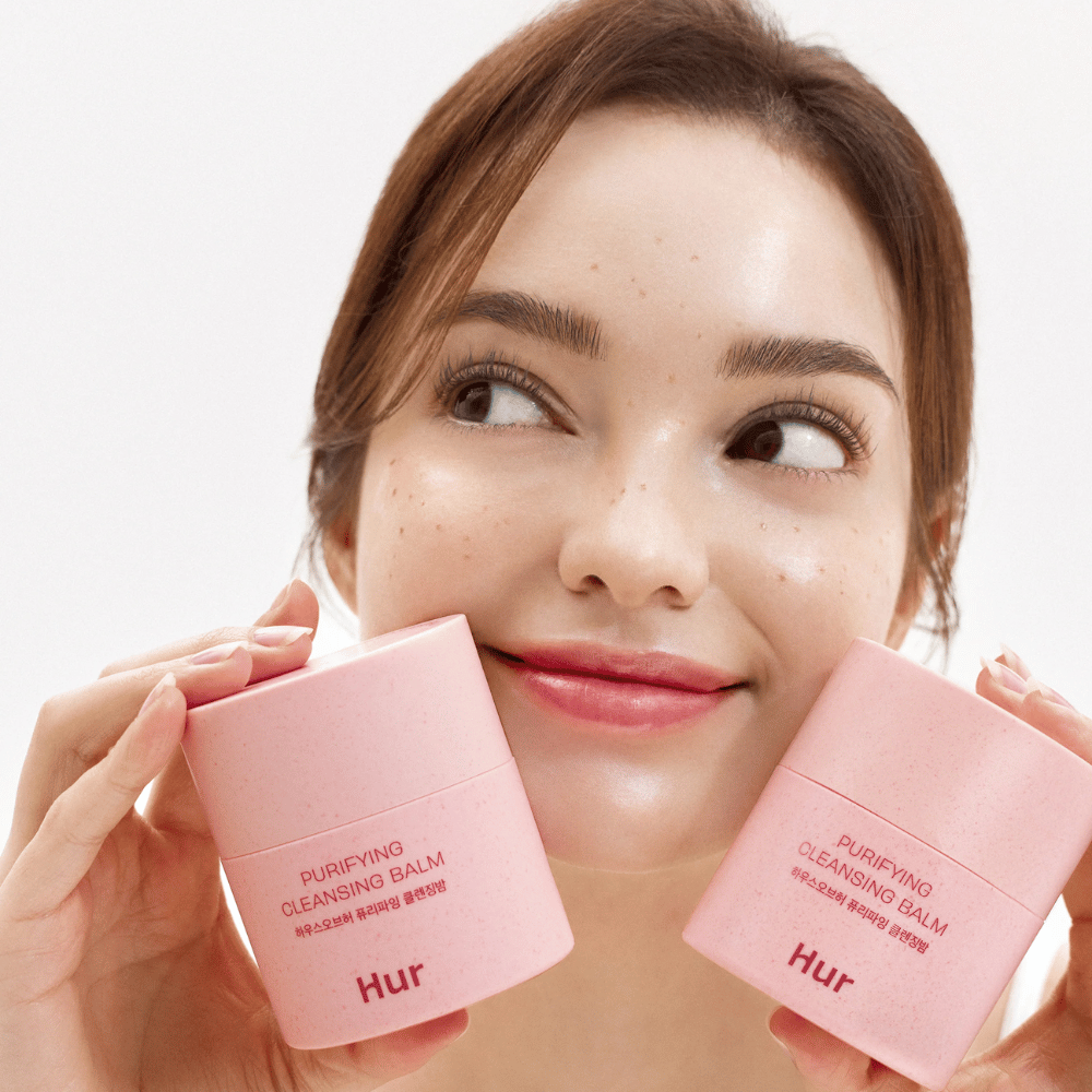 Mannequin tenant deux pots Comment Purifying Cleansing Balm. Baume nettoyant doux qui convient aux peaux sensibles et donne une sensation de fraîcheur et d'hydratation après le nettoyage.