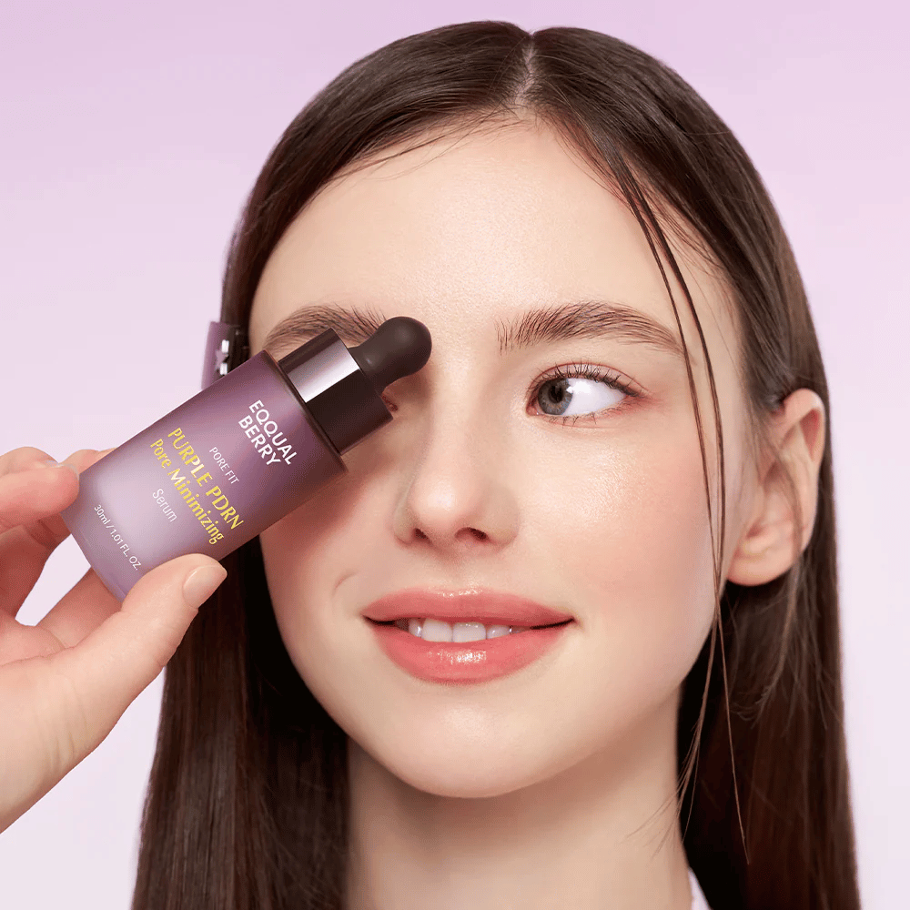 Jeune femme à la peau lisse tenant une bouteille d'Equal Berry Purple PDRN Pore Minimizing Serum contre son front, sur fond violet clair.