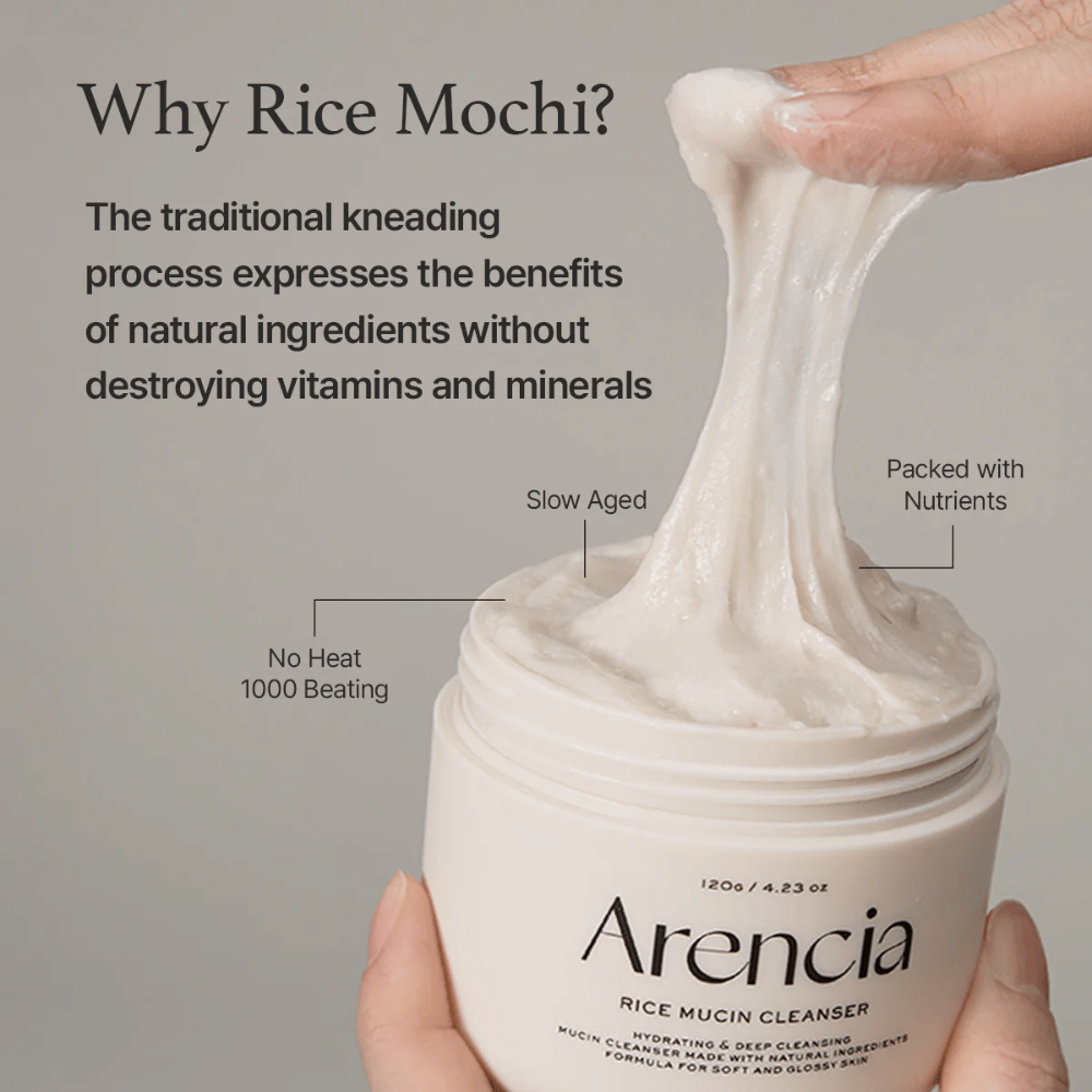 Main qui soulève une crème nettoyante blanche et élastique d'un pot marqué "Arencia Rice Mucin Cleanser". Le texte décrit le pétrissage traditionnel qui préserve les nutriments sans détruire les vitamines et les minéraux.