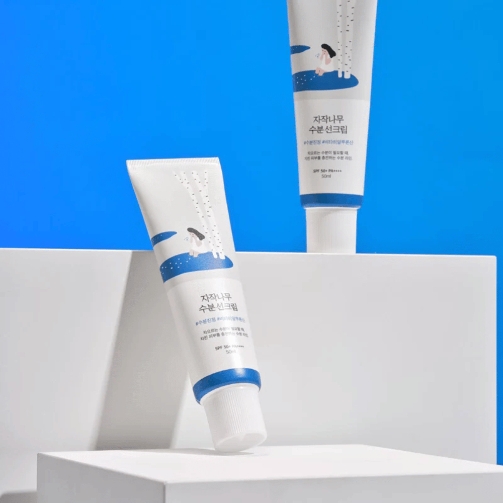 Deux tubes de Round Lab Birch Juice Moisturizing Sunscreen SPF50+ PA++++ 50ml posés sur un fond bleu.