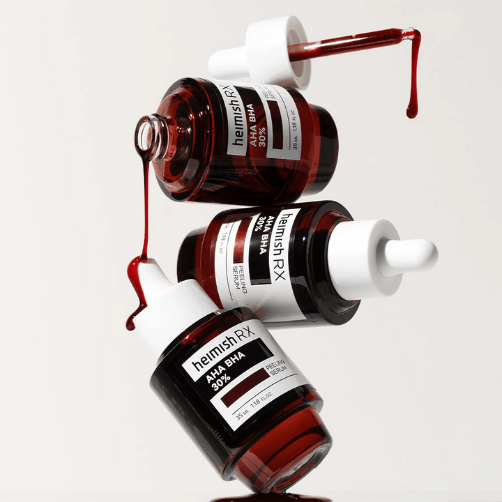 Trois bouteilles de Heimish RX AHA BHA 30% Peeling Serum dans une composition dynamique, avec du sérum rouge coulant des pipettes.