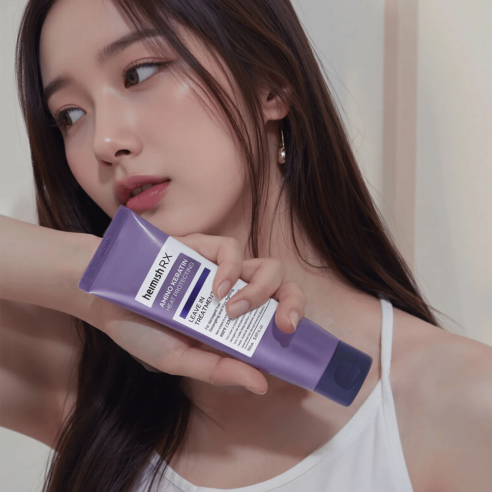 Femme aux cheveux longs et brillants tenant Heimish RX Amino Keratin Leave-In Treatment – montre le produit comme une étape de soin et de protection thermique dans la routine capillaire.