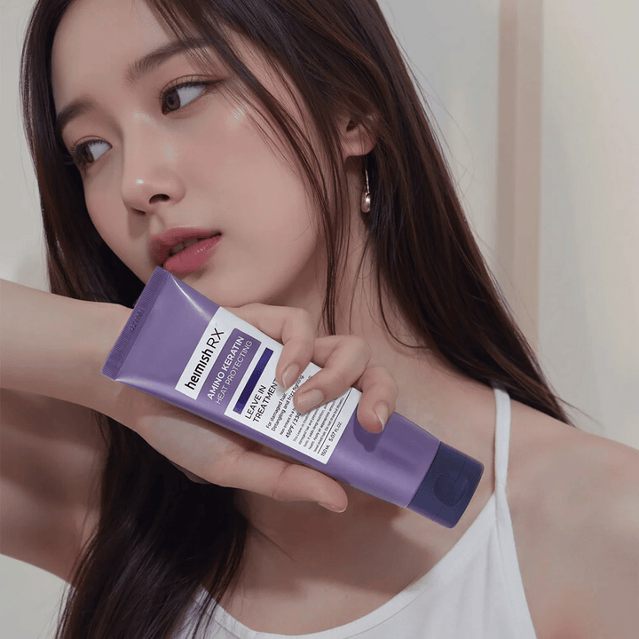 Femme aux cheveux longs et brillants tenant Heimish RX Amino Keratin Leave-In Treatment – montre le produit comme une étape de soin et de protection thermique dans la routine capillaire.