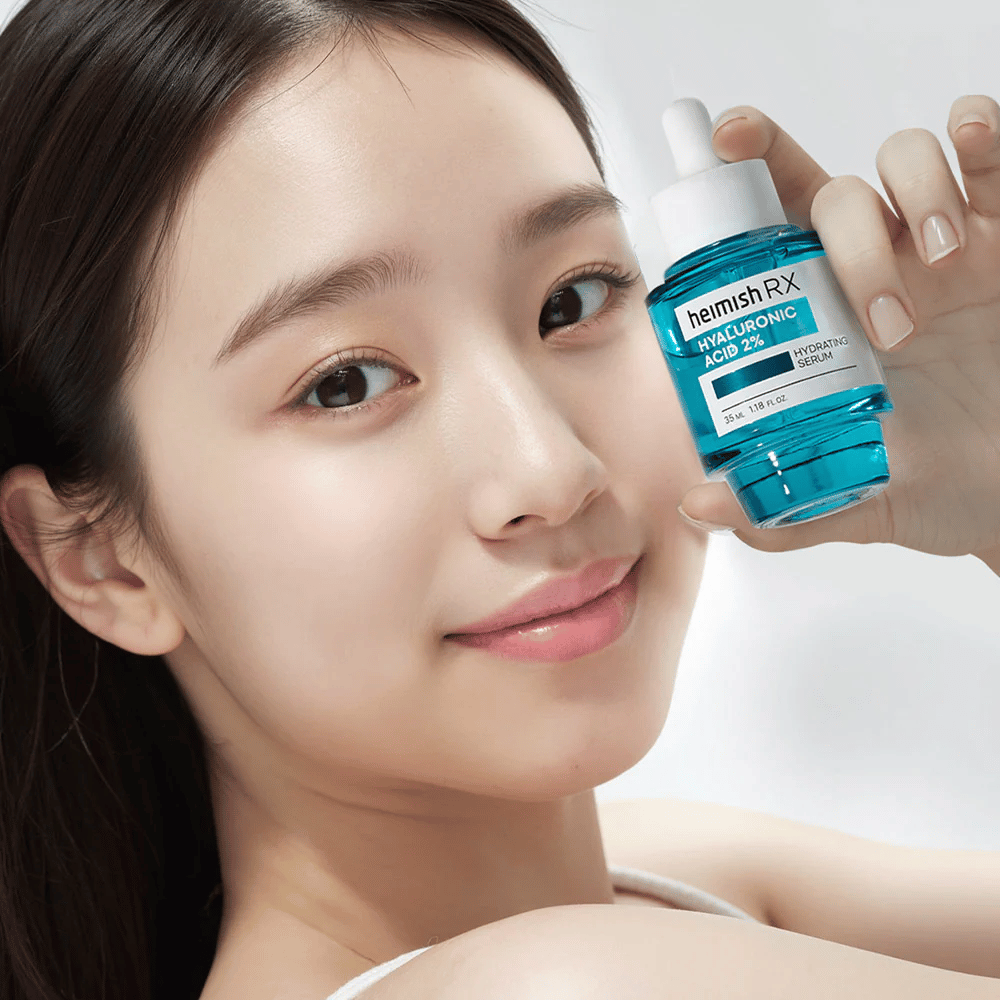 Femme souriante avec une peau éclatante tenant une bouteille de Heimish RX Hyaluronic Acid 2% Hydrating Serum, mettant en avant ses propriétés hydratantes.