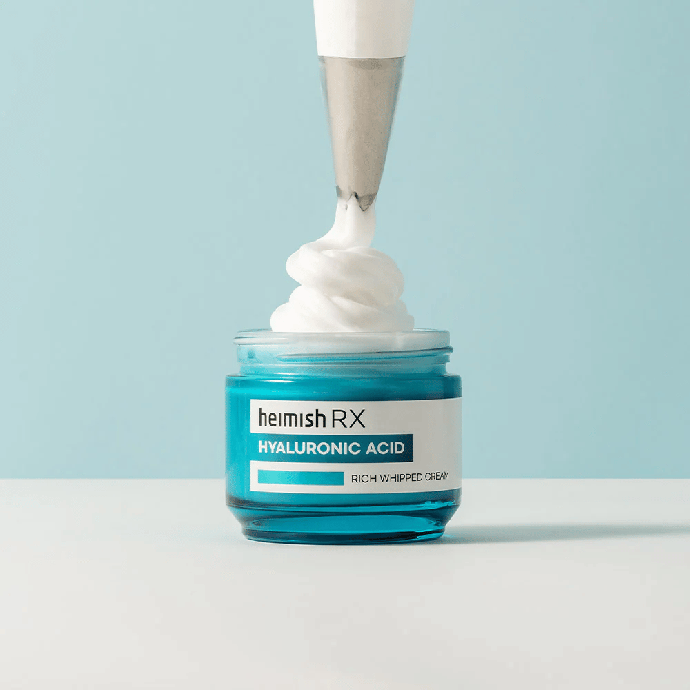 Heimish RX Hyaluronic Acid Rich Whipped Cream dans un pot en verre bleu, où une poche à douille applique la crème onctueuse. Une crème pour le visage hydratante avec de l'acide hyaluronique pour une hydratation intense et une peau douce et pulpeuse.