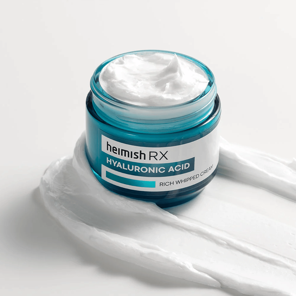 Heimish RX Hyaluronic Acid Rich Whipped Cream dans un pot en verre bleu avec une consistance riche et onctueuse, étalée sur un fond blanc. Crème pour le visage intensément hydratante avec de l'acide hyaluronique pour une hydratation profonde et une peau douce.