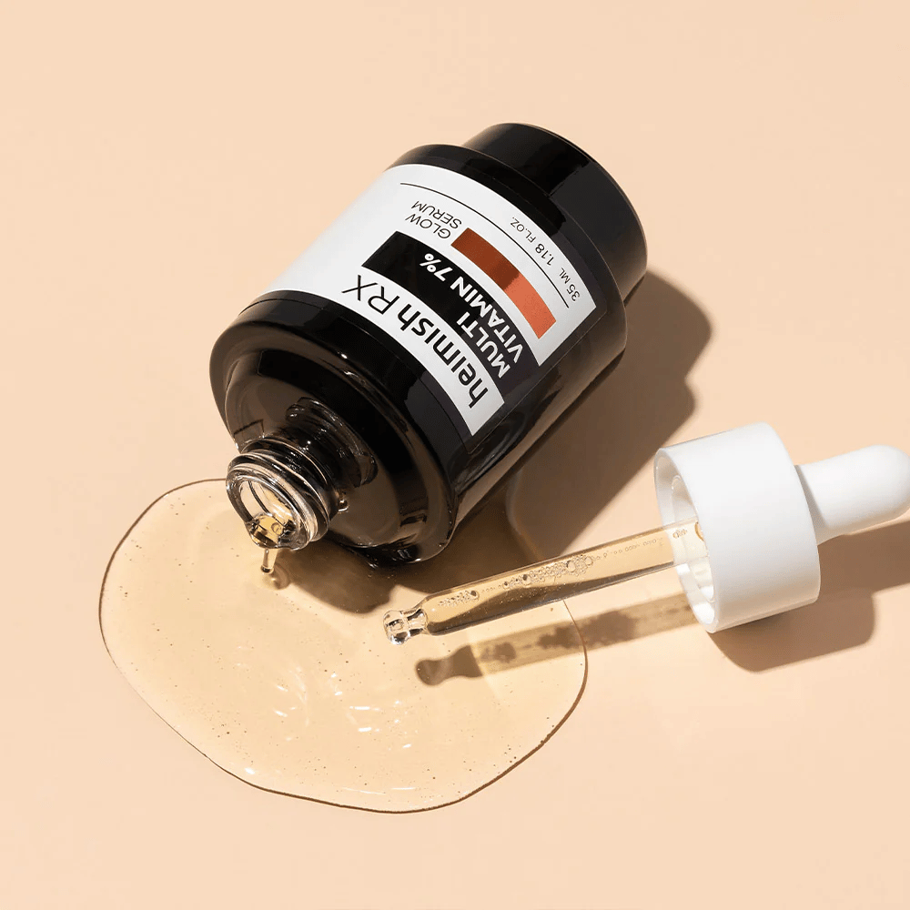 Heimish RX Multi Vitamin 7% Glow Serum posé sur un fond beige avec du sérum répandu autour de la bouteille et une pipette remplie de produit, mettant en valeur sa formule riche en nutriments.