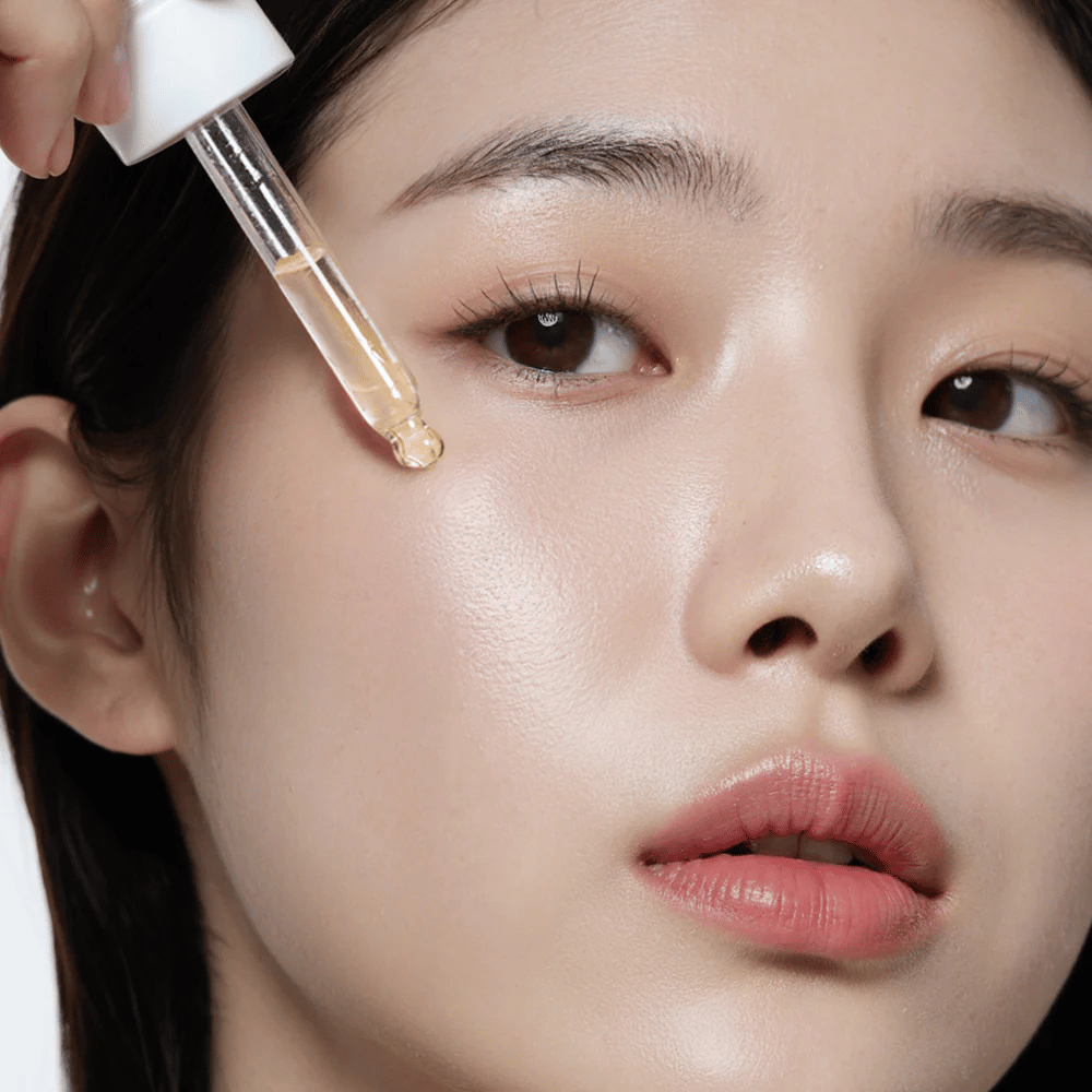 Gros plan d'une femme avec une peau lisse et hydratée appliquant Heimish RX Multi Vitamin 7% Glow Serum avec une pipette pour un éclat et une nutrition supplémentaires.