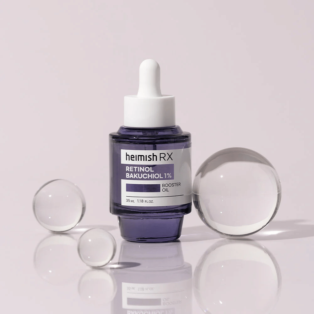 Heimish RX Retinol Bakuchiol Booster Oil 1% dans une élégante bouteille en verre violet avec pipette. L'huile est placée sur une surface réfléchissante avec des billes de verre autour, donnant une sensation luxueuse et moderne.