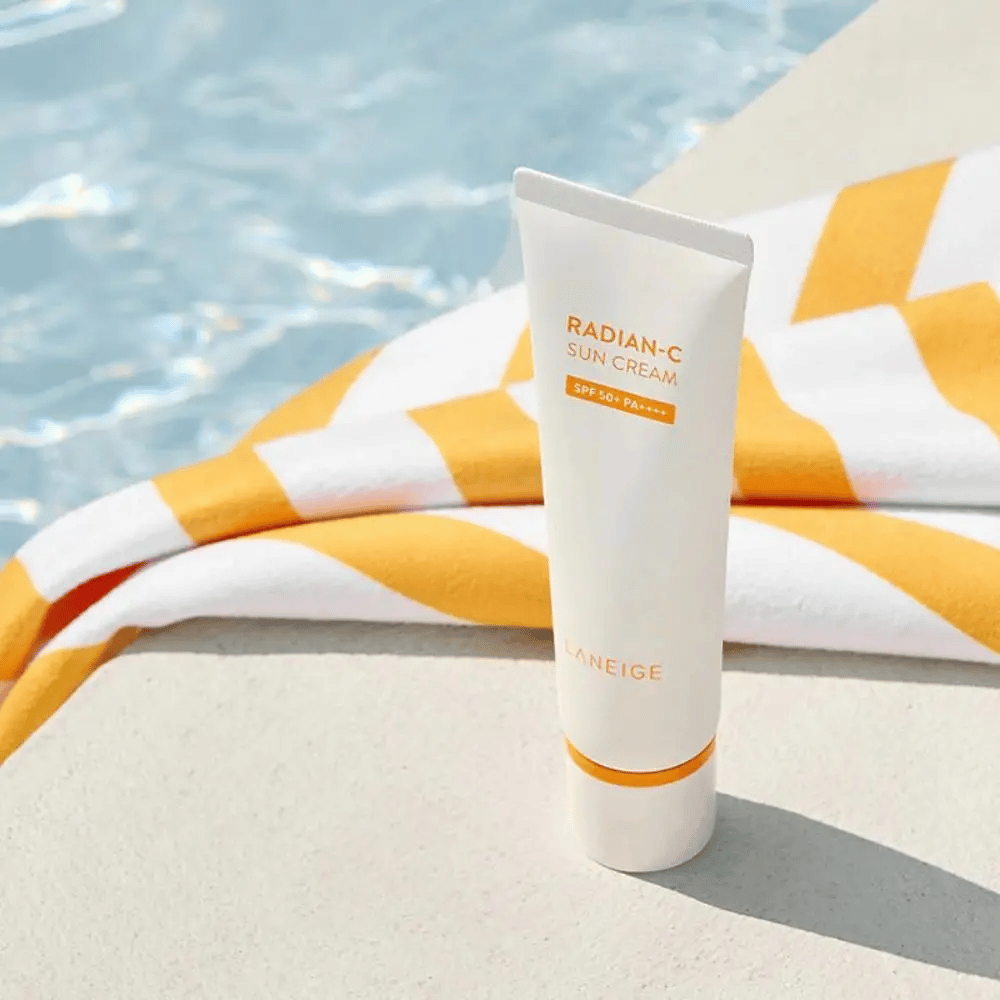 LANEIGE Radian-C Sun Cream se tient au bord d'une piscine avec une serviette rayée jaune et blanche en arrière-plan.