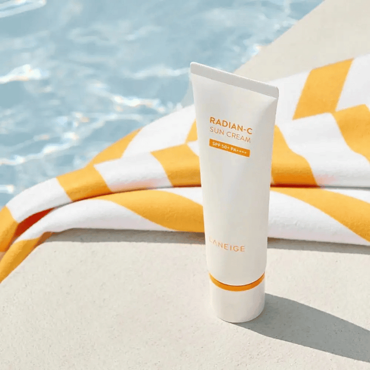 LANEIGE Radian-C Sun Cream se tient au bord d'une piscine avec une serviette rayée jaune et blanche en arrière-plan.