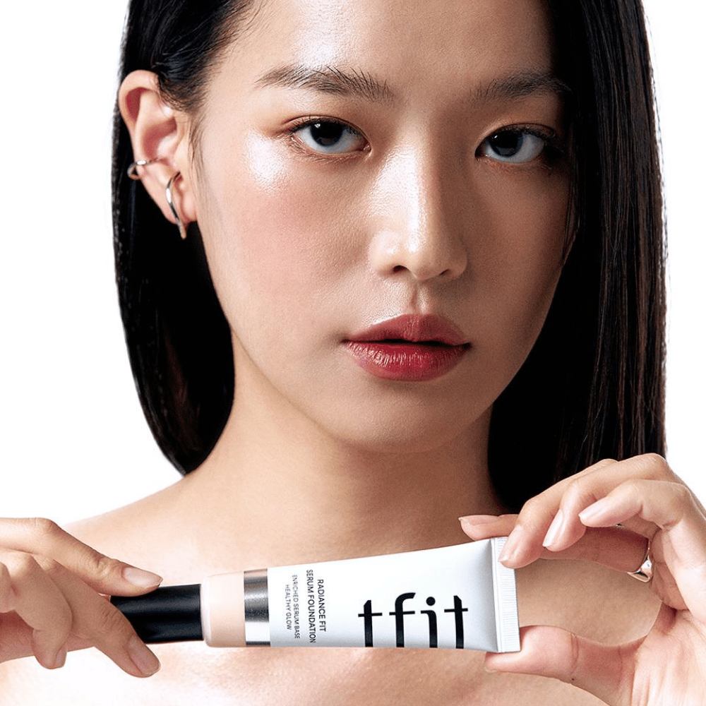 Modèle à la peau lisse et brillante tenant TFIT Radiance Fit Serum Foundation, ce qui met en valeur la finition naturelle et l'éclat du produit.