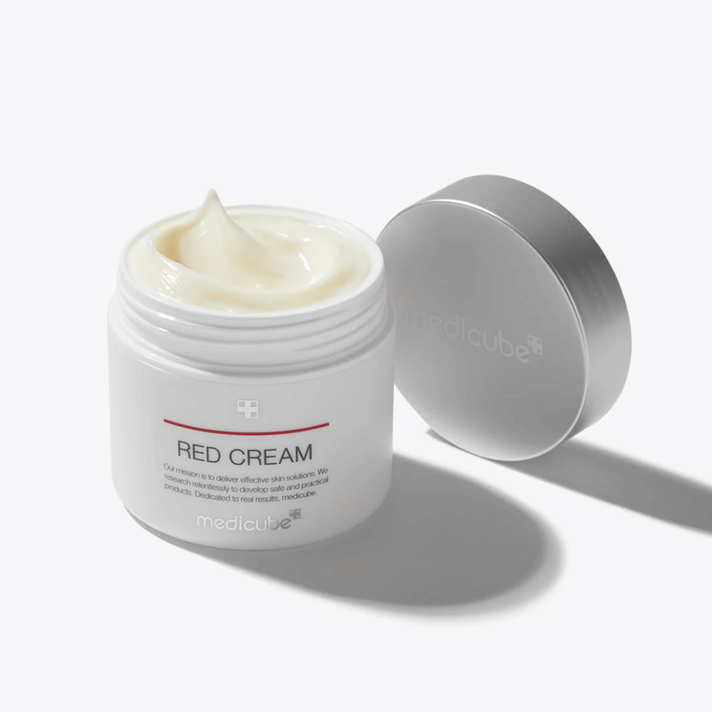 Pot ouvert avec medicube Red Cream 50ml – une crème pour le visage jaune pâle dans un emballage blanc avec un couvercle argenté, conçue pour les peaux sujettes à l'acné.