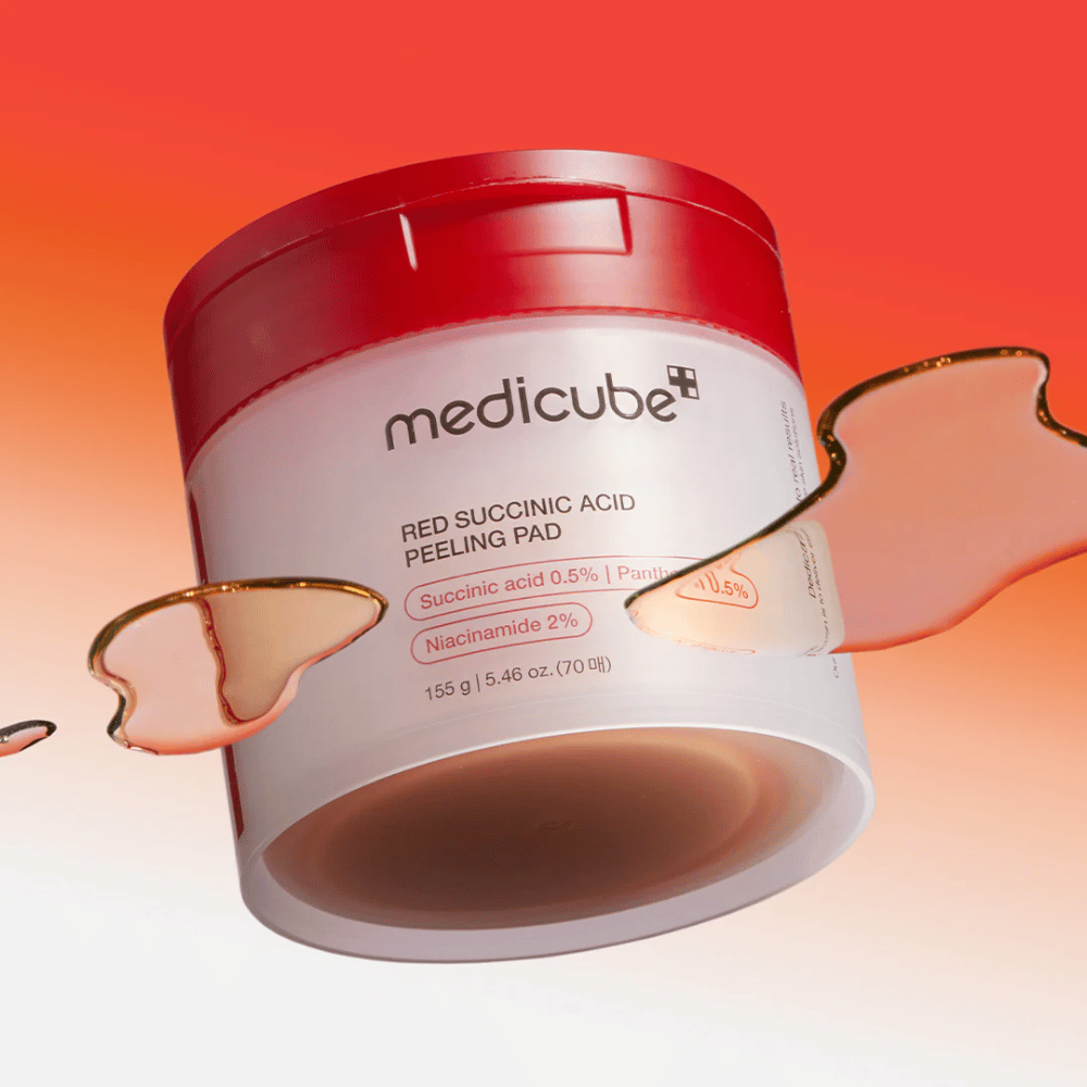 Medicube Red Succinic Acid Peeling Pad dans un pot blanc et rouge, placé sur un fond dégradé rouge et orange. Le produit contient de l'acide succinique et de la niacinamide pour l'exfoliation et l'amélioration de la peau. Texture liquide visible autour du pot.