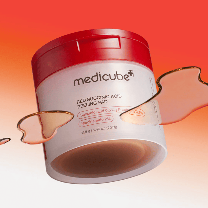 Medicube Red Succinic Acid Peeling Pad dans un pot blanc et rouge, placé sur un fond dégradé rouge et orange. Le produit contient de l'acide succinique et de la niacinamide pour l'exfoliation et l'amélioration de la peau. Texture liquide visible autour du pot.