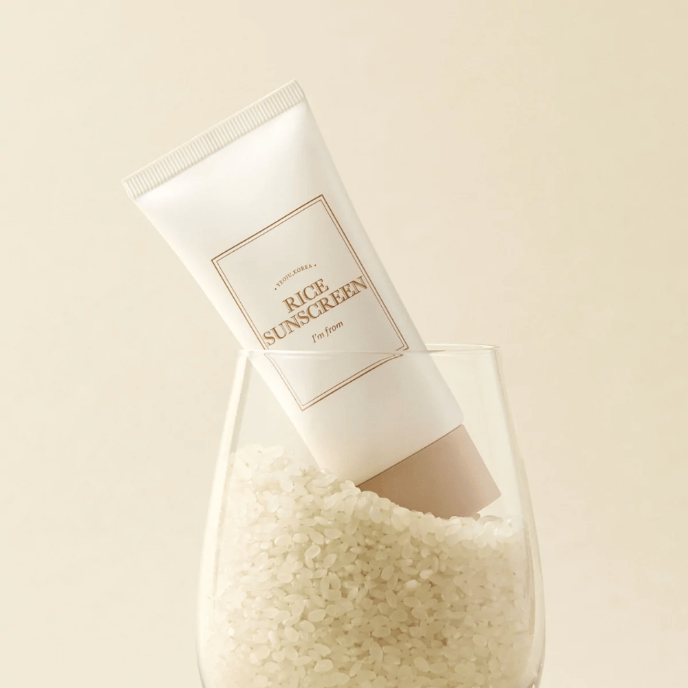 Tube avec "I'm from" Rice Sunscreen, SPF50+ PA++++, placé dans un verre avec des grains de riz.