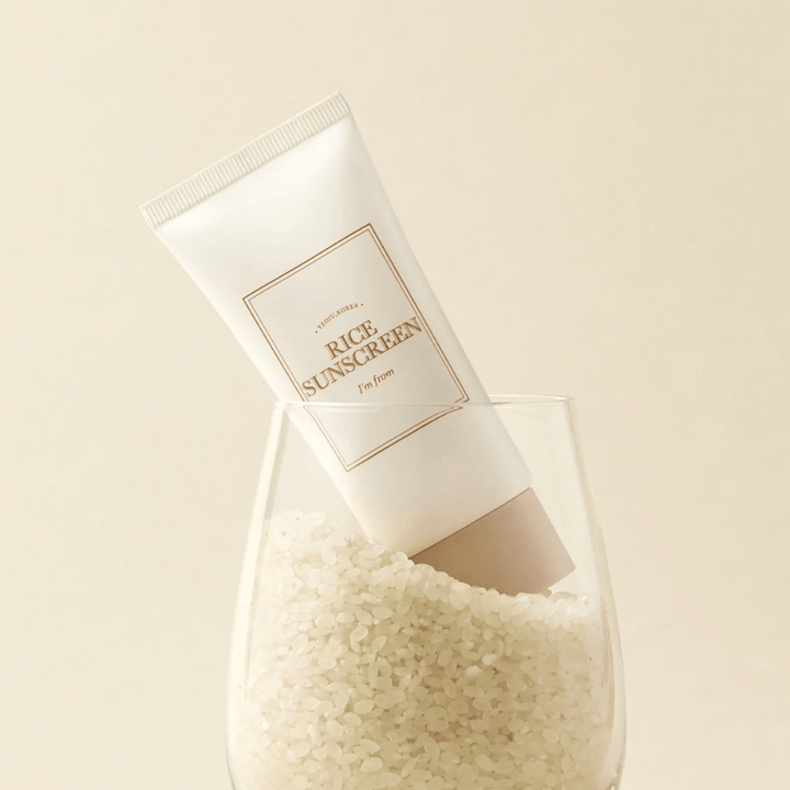 Tube avec "I'm from" Rice Sunscreen, SPF50+ PA++++, placé dans un verre avec des grains de riz.