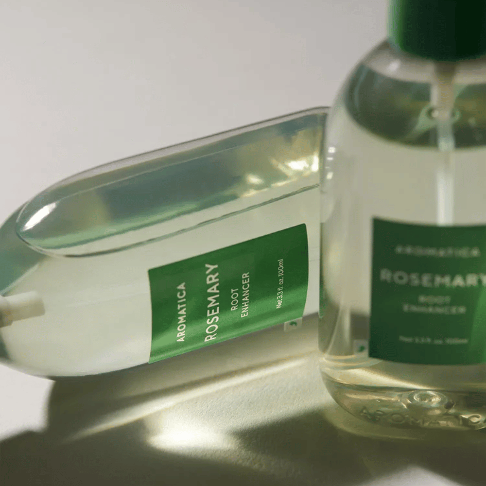Deux bouteilles de AROMATICA Rosemary Root Enhancer avec capuchon de protection transparent et étiquette verte. Gros plan mettant en avant le design premium du produit et son concept de soin capillaire naturel.