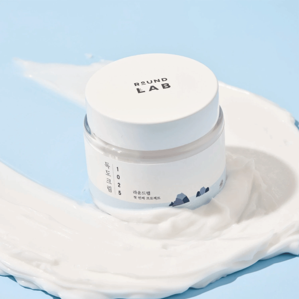 Un pot de Round Labs 1025 Dokdo Cream 80 ml qui offre une hydratation, placé sur un fond bleu vif.