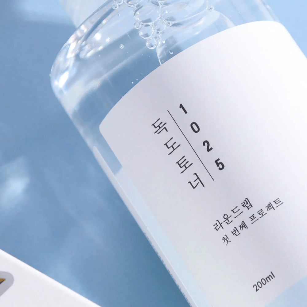 Gros plan d'une bouteille transparente Round Lab 1025 Dokdo Toner, remplie de liquide clair, sur fond bleu.