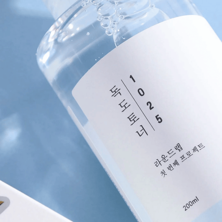 Gros plan d'une bouteille transparente Round Lab 1025 Dokdo Toner, remplie de liquide clair, sur fond bleu.