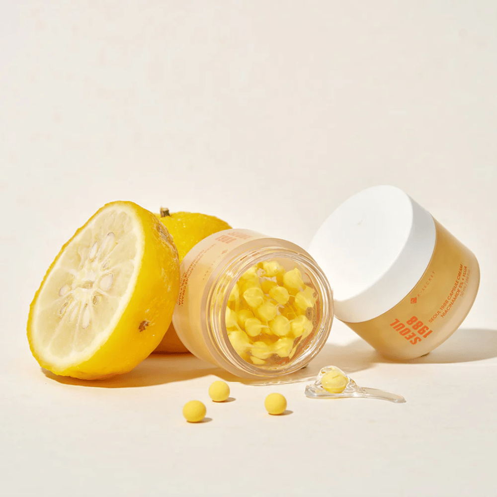 Pot ouvert avec des capsules jaunes à côté d'un fruit de yuja coupé en deux qui met en valeur la formule riche en vitamine C.