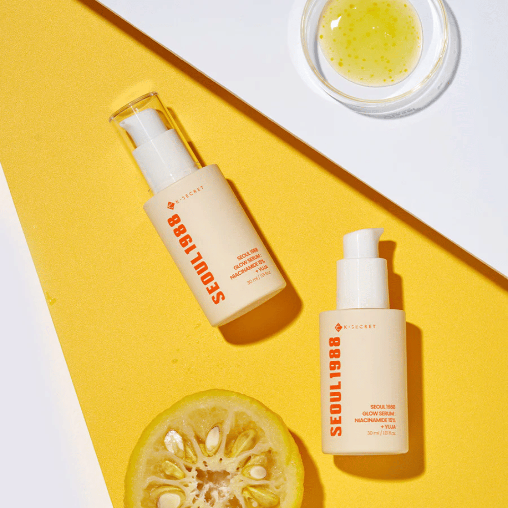 Deux bouteilles Séoul 1988 Glow Serum placées sur un fond jaune avec un bol de sérum jaune et un agrume coupé en deux.