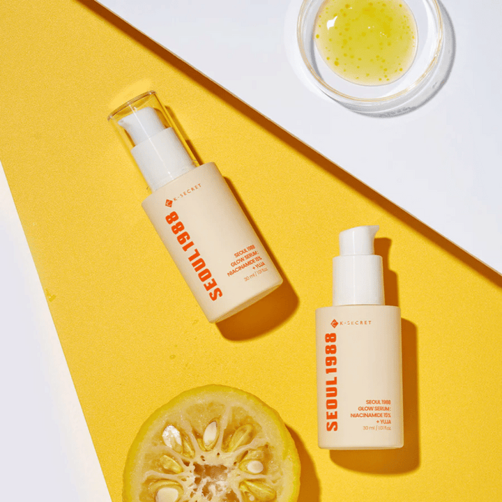Deux bouteilles Séoul 1988 Glow Serum placées sur un fond jaune avec un bol de sérum jaune et un agrume coupé en deux.