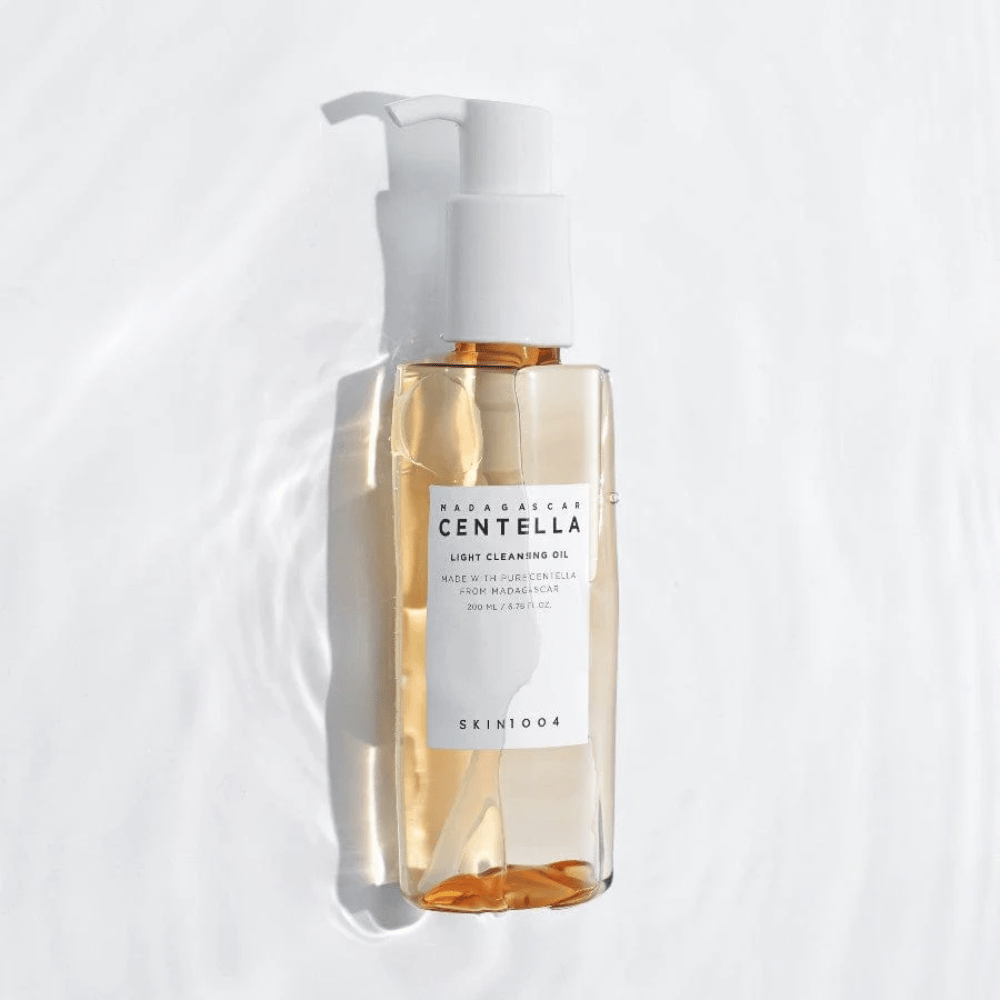 SKIN1004 Madagascar Centella Light Cleansing Oil sur fond blanc avec des reflets d'eau doux qui mettent en valeur le flacon transparent et le contenu doré.