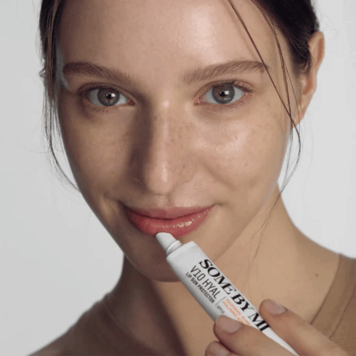 Une femme tient un tube V10 Hyal Lip Sun Protector SPF15 7ml de baume à lèvres pour la protection solaire et l'hydratation, de SOME BY MI.