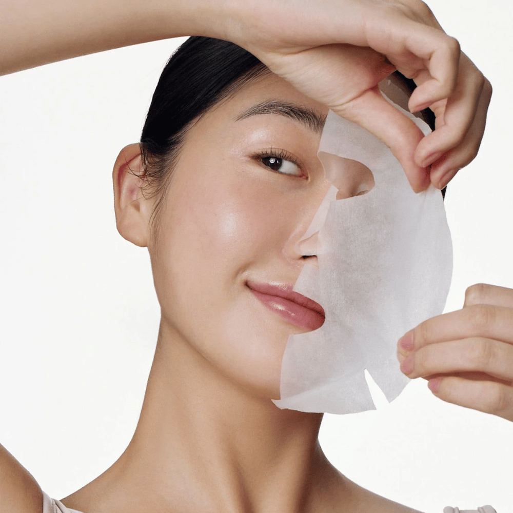 Cette image montre une personne utilisant un masque facial, spécifiquement "Galactomyces Glutathione Daily Mask" de Some By Mi. Le masque éclaircit la peau et donne un éclat radieux tout en nourrissant et hydratant en profondeur grâce à des ingrédients tels que le glutathion et la vitamine C.