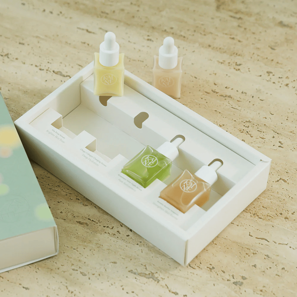 Quatre flacons de sérum colorés de KAINE Serum Discovery Kit avec bouchon pipette, conçus pour répondre à différents besoins de la peau dans un emballage minimaliste et élégant.