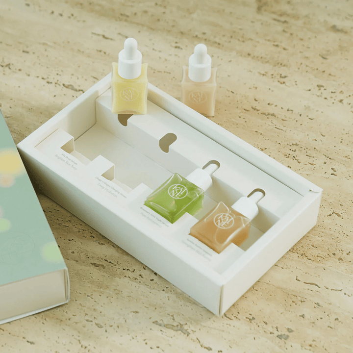 Quatre flacons de sérum colorés de KAINE Serum Discovery Kit avec bouchon pipette, conçus pour répondre à différents besoins de la peau dans un emballage minimaliste et élégant.
