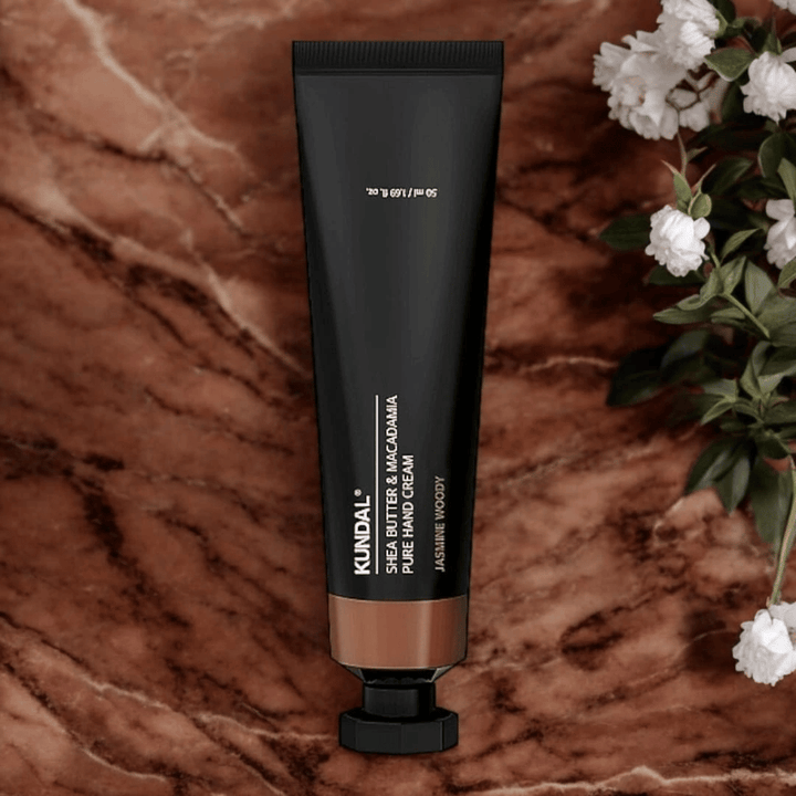 KUNDAL Shea Butter & Macadamia Pure Hand Cream Jasmine Woody placé sur du marbre avec des fleurs – crème pour les mains nourrissante qui soigne les mains sèches et offre un élégant parfum jasmin boisé.