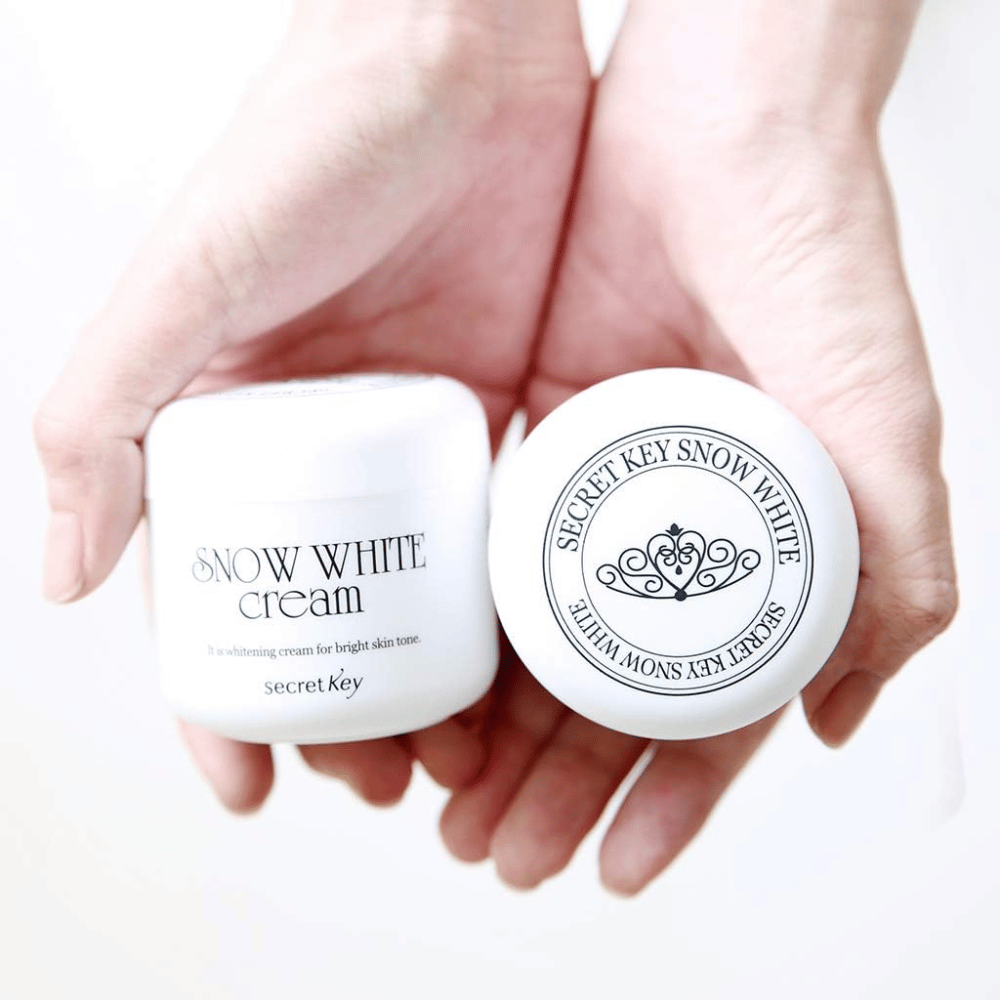 Deux pots de Secret Key Snow White Cream tenus dans les mains, un montrant le couvercle et un montrant l'avant.