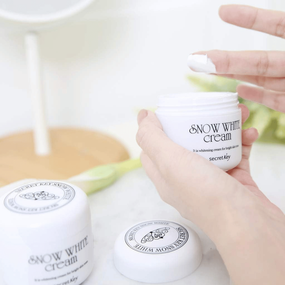 Main prenant de la crème blanche d'un pot Secret Key Snow White Cream sur une coiffeuse.