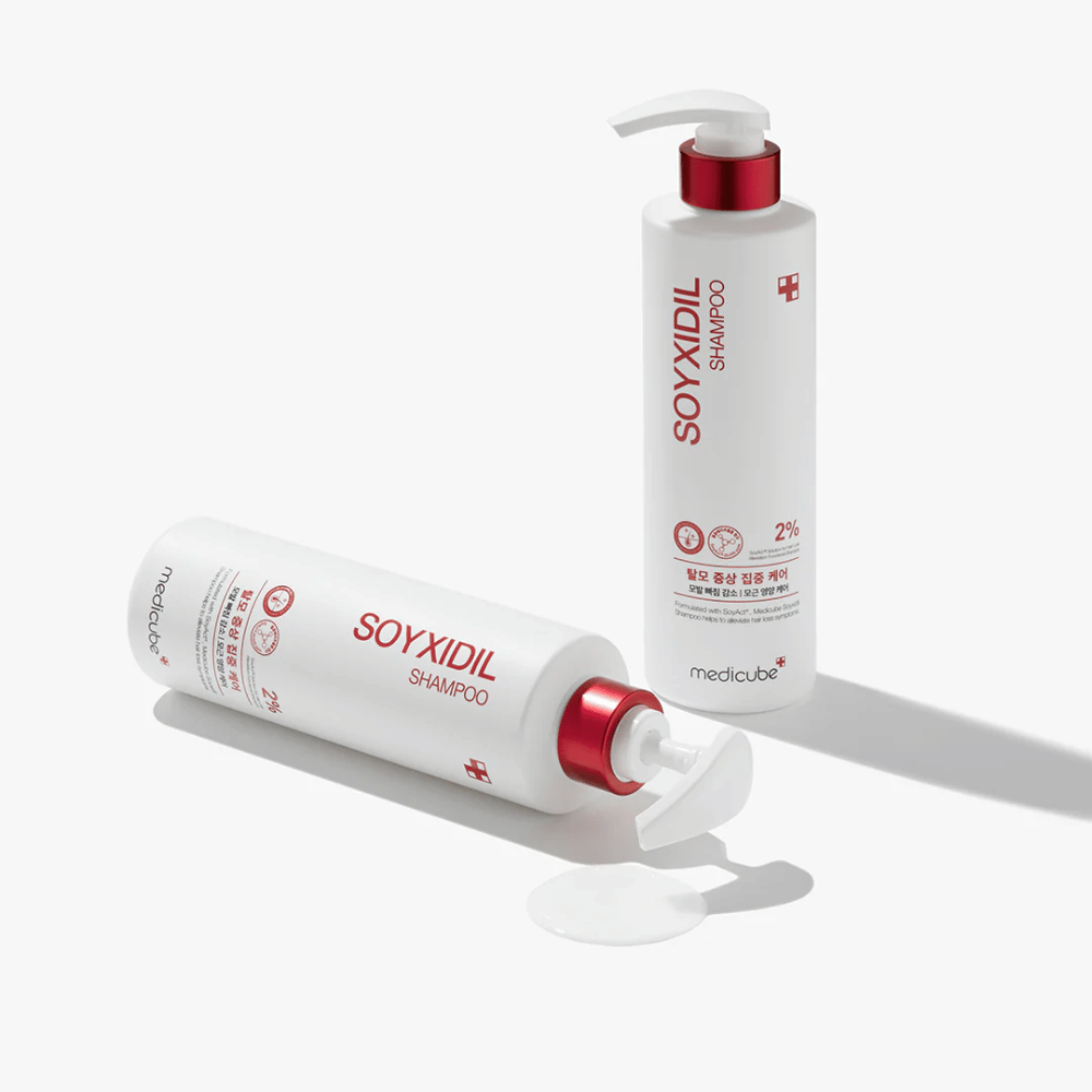 Deux bouteilles de Medicube Soyxidil Shampoo en design blanc et rouge, une debout et une couchée avec du shampooing renversé à côté.