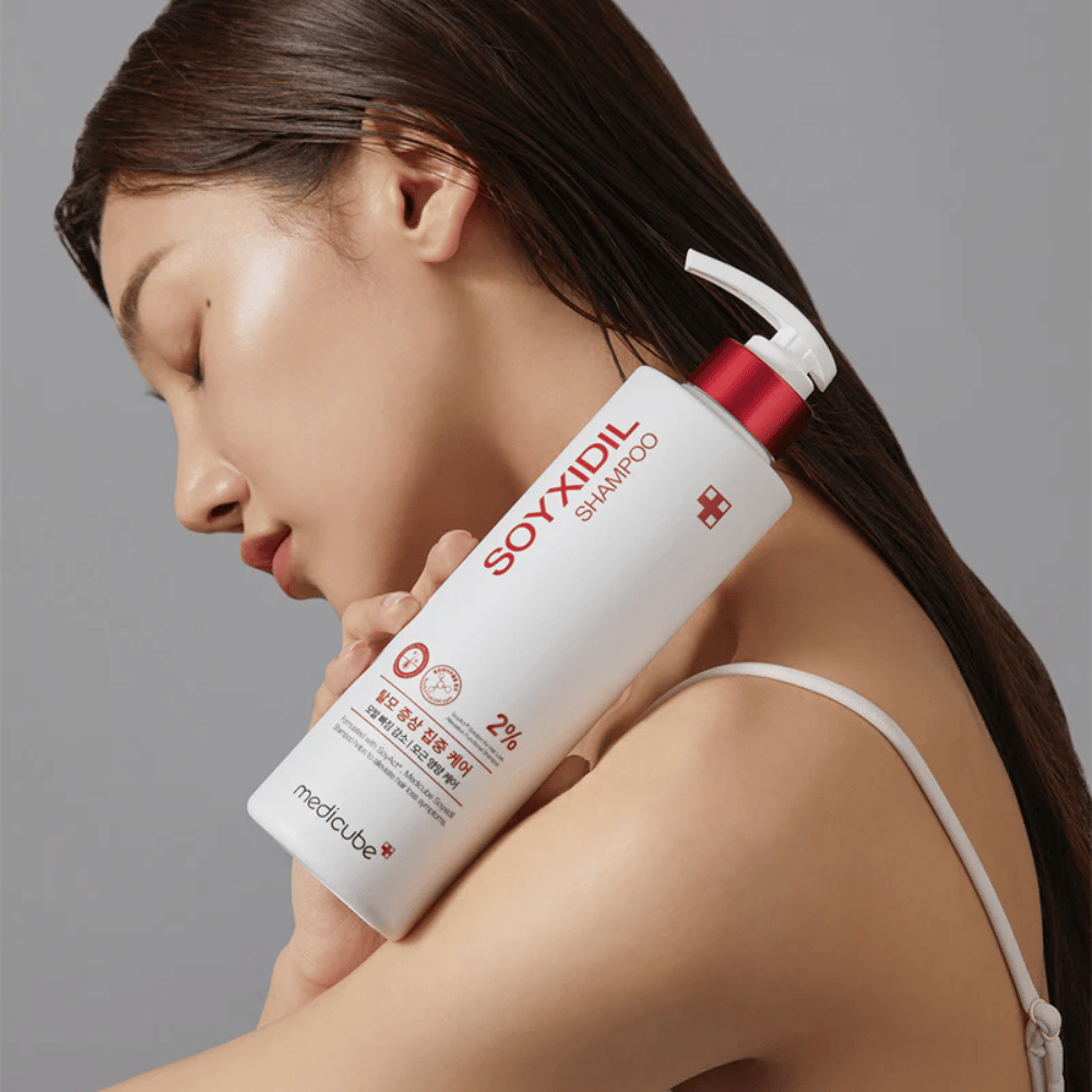 Femme aux longs cheveux appuyant sa tête contre une bouteille de Medicube Soyxidil Shampoo, qui renforce le cuir chevelu et prévient la chute des cheveux.