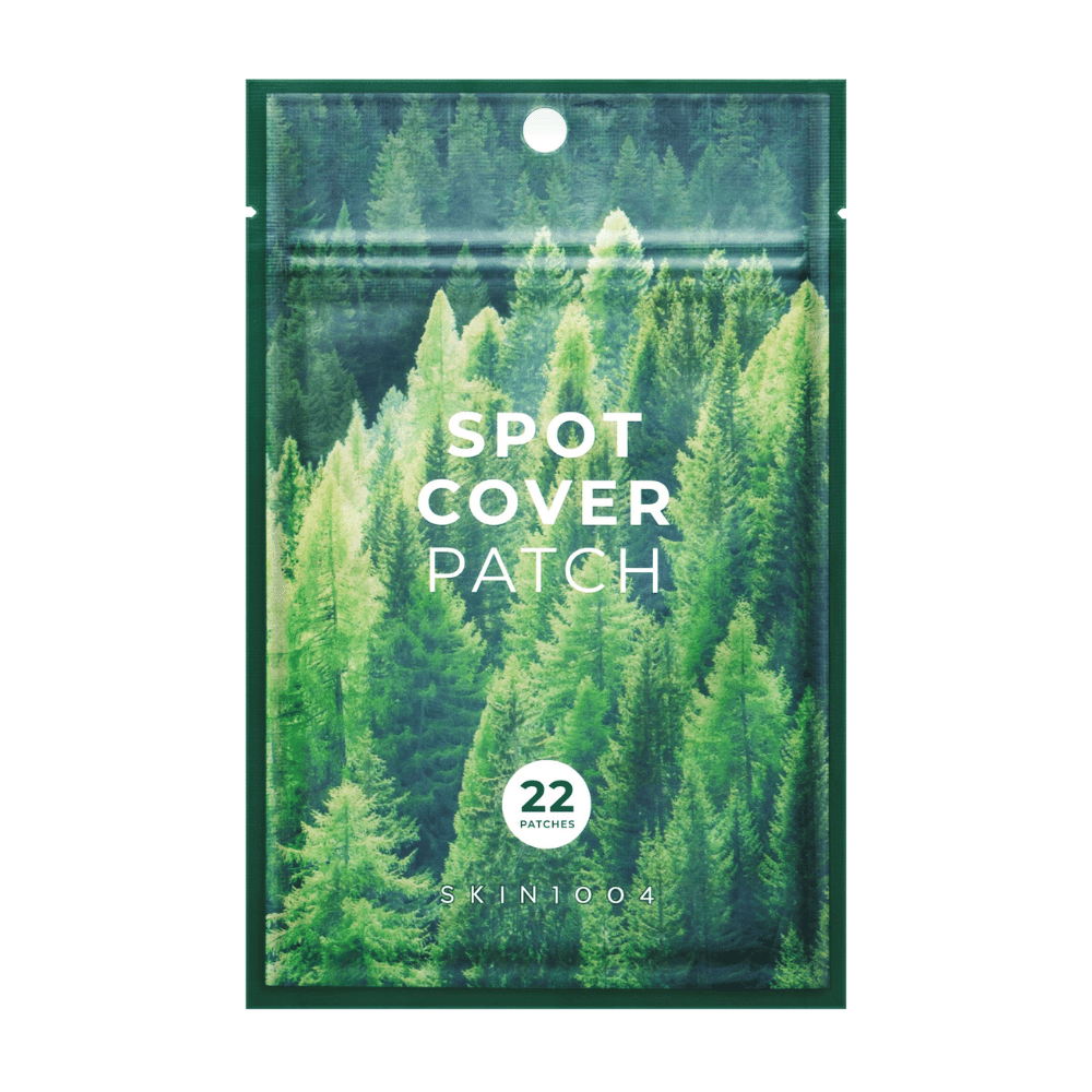 Emballage avec "Spot Cover Patch" contenant 22 pansements, conçu avec un motif de forêt verte. Le texte "SPOT COVER PATCH" est imprimé en blanc sur le devant, et un cercle indique le nombre de pansements. Le produit est de la marque SKIN1004.