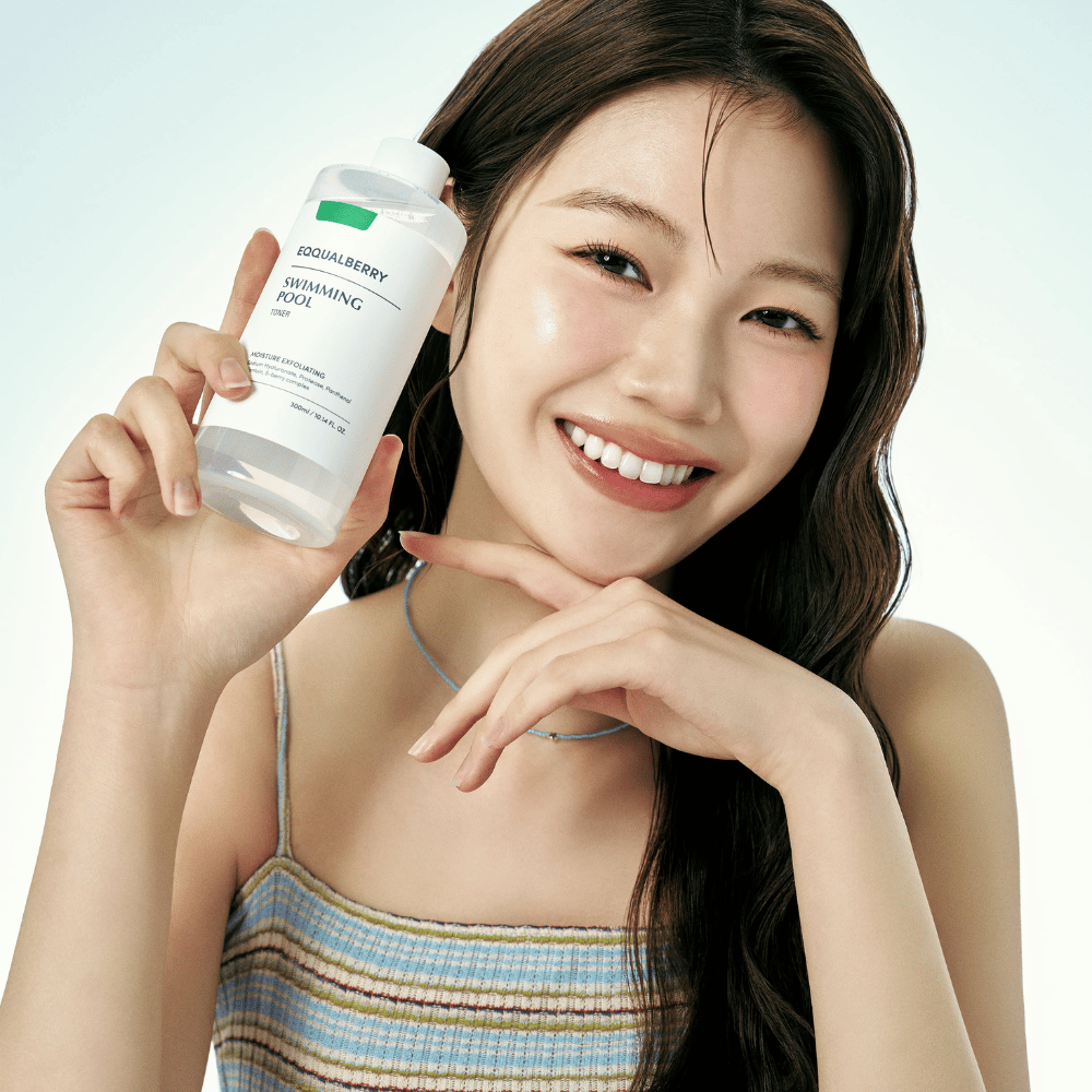 Femme souriante avec une peau radieuse tenant Equalberry Swimming Pool Toner. Look frais et naturel avec un maquillage léger et une tenue estivale dans des tons bleus.