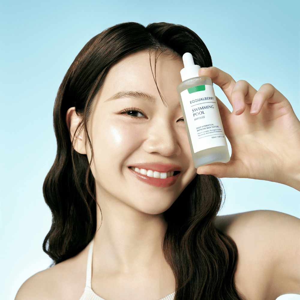 Une femme souriante tient Eqqualberry Swimming Pool Ampoule, un produit de soin hydratant intense, sur un fond bleu clair.