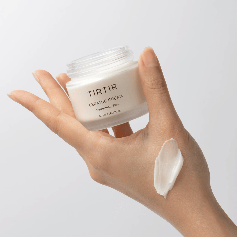 Une main tient un pot avec TIRTIR Ceramic Cream. Sur le dos de la main, une quantité de crème a été appliquée. La crème semble être épaisse et hydratante. L'emballage indique que le contenu est pour "Refreshing Skin" et la quantité est de 50 ml / 1.69 fl oz.