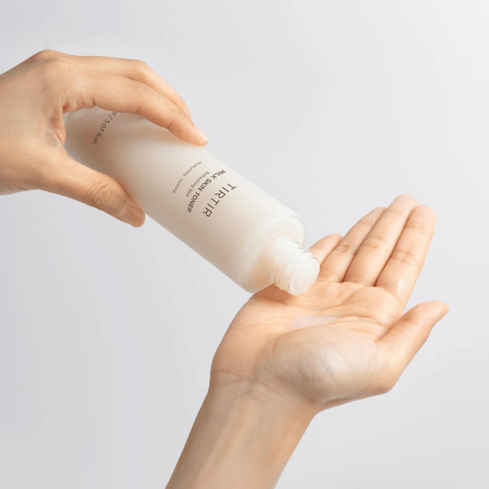 L'image montre une personne versant un liquide laiteux d'une bouteille marquée "TIRTIR Milk Skin" dans la paume de la main. Le produit semble être un tonique pour la peau ou une lotion hydratante.