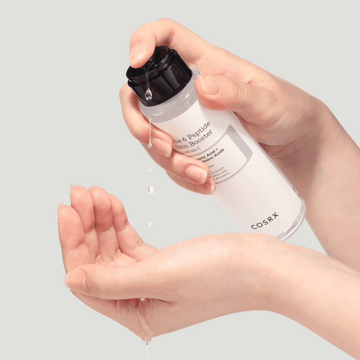 Mains versant un produit de soin de la peau d'une bouteille transparente avec le texte "The Peptide Skin Booster".
