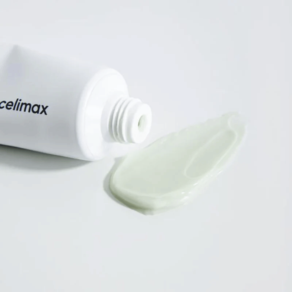 Celimax Noni Energy Repair Cream dans un tube blanc avec une petite quantité de crème vert clair étalée à côté du tube sur une surface blanche. La crème est destinée à nourrir et réparer la peau.