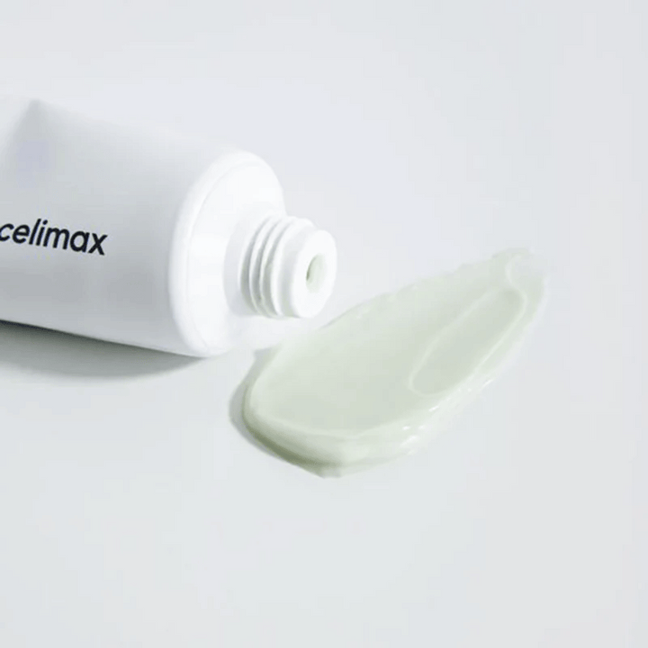 Celimax Noni Energy Repair Cream dans un tube blanc avec une petite quantité de crème vert clair étalée à côté du tube sur une surface blanche. La crème est destinée à nourrir et réparer la peau.