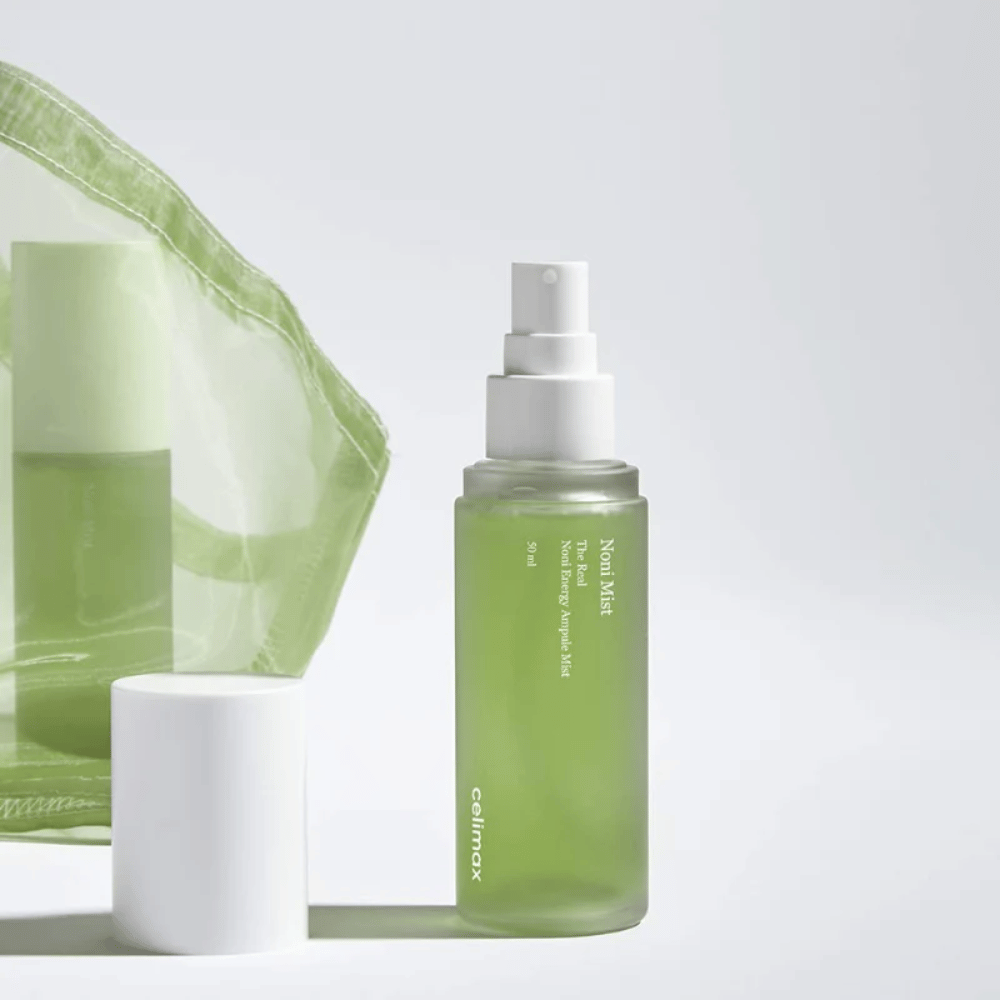 Une bouteille de Celimax Noni Mist, un flacon pulvérisateur vert avec une pompe blanche, se tient à côté d'un bouchon. Le produit est emballé dans un sac en plastique transparent et est commercialisé comme Noni Energy Ampule Mist.