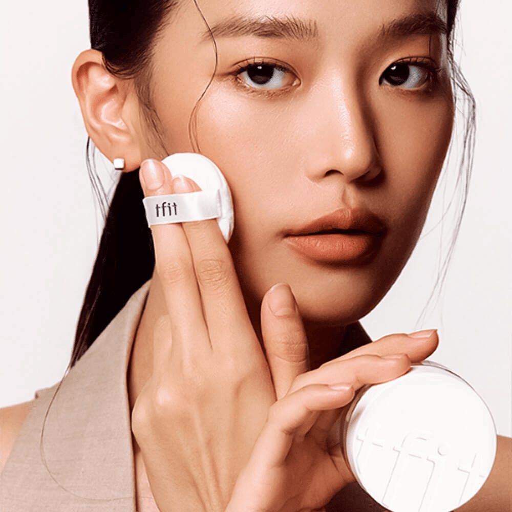 Femme appliquant TFIT Translucent Set Finishing Powder #02 Beige Peau avec une houppette, tenant un boîtier à poudre blanc avec le logo TFIT.