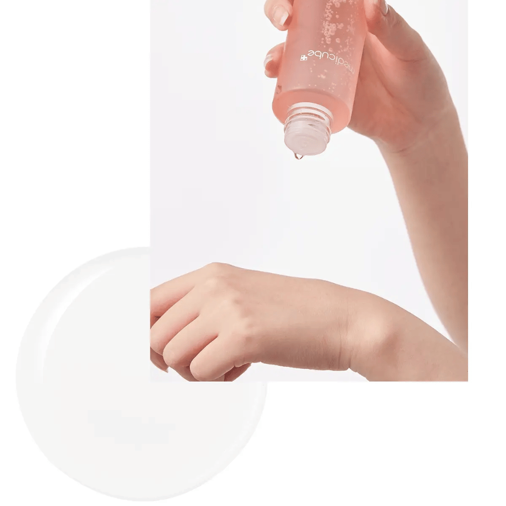 Main versant Medicube Triple Collagen Toner 4.0 d'une bouteille rose sur la peau, montrant la consistance hydratante.
