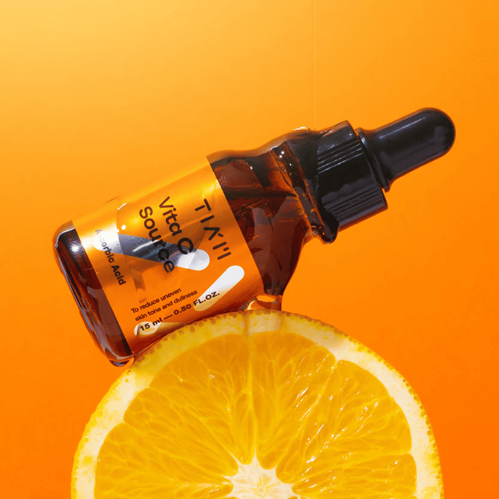 TIA'M Vita C Source-bouteille placée contre une orange et un fond orange symbolisant la fraîcheur et l'effet antioxydant de la vitamine C.